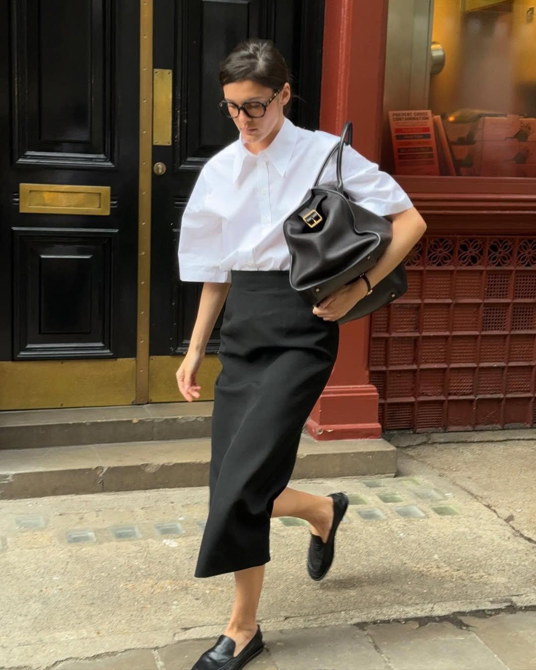 Valeria in a black pencil skirt and white blouse with bowler bag