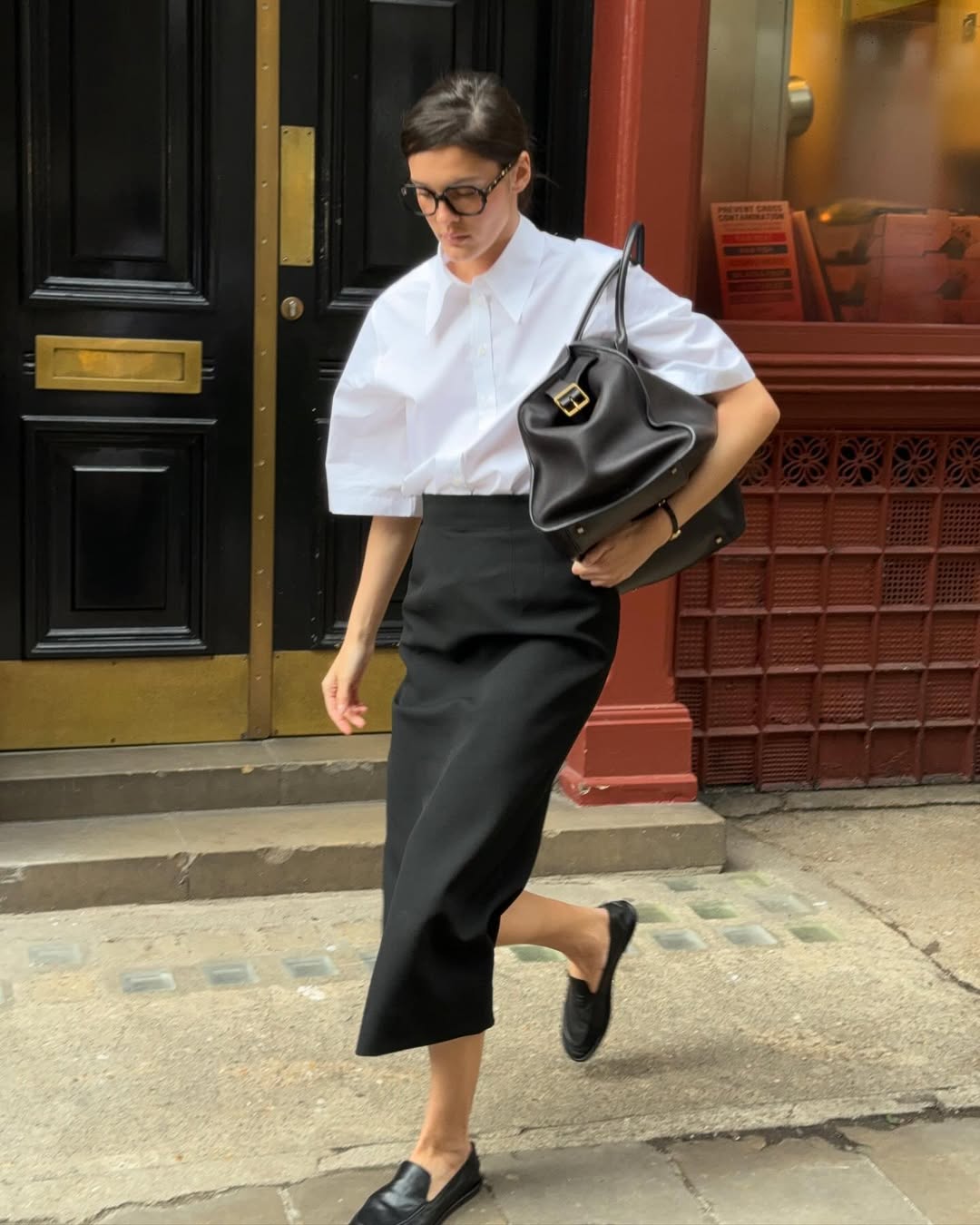 Valeria in a black pencil skirt and white blouse with bowler bag