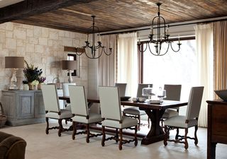 dining room with pale stone floor and dark wood ceiling chandeliers dark table and white leather style chairs