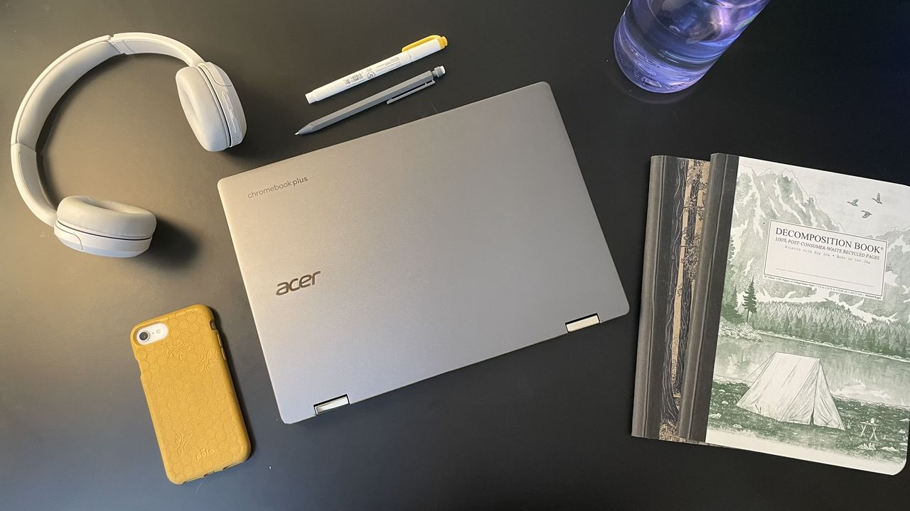 The Acer Chromebook Plus Spin 714 on a black table with headphones, a phone, pens, and notebooks around it.