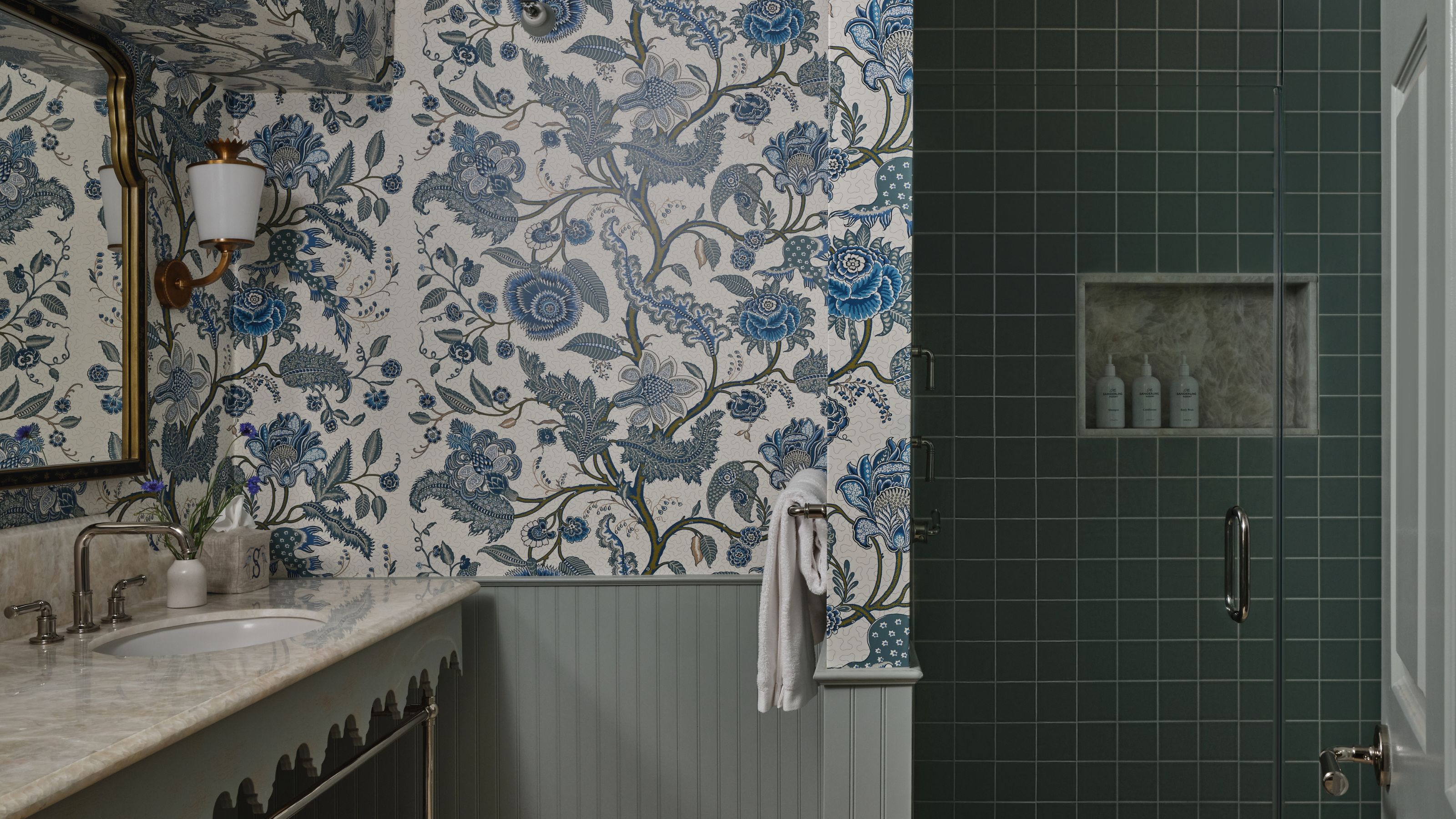 Elegant bathroom featuring blue and white floral wallpaper, a marble vanity, sage green beadboard, and a dark green tiled walk-in shower.