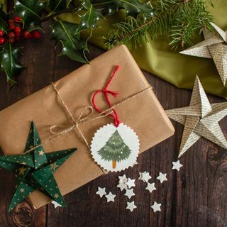 christmas gift wrapped in brown paper tied up with string, with paper stars and holly placed beside it