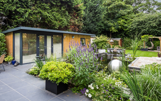 contemporary garden room with black patio, water feature, lush green planted areas
