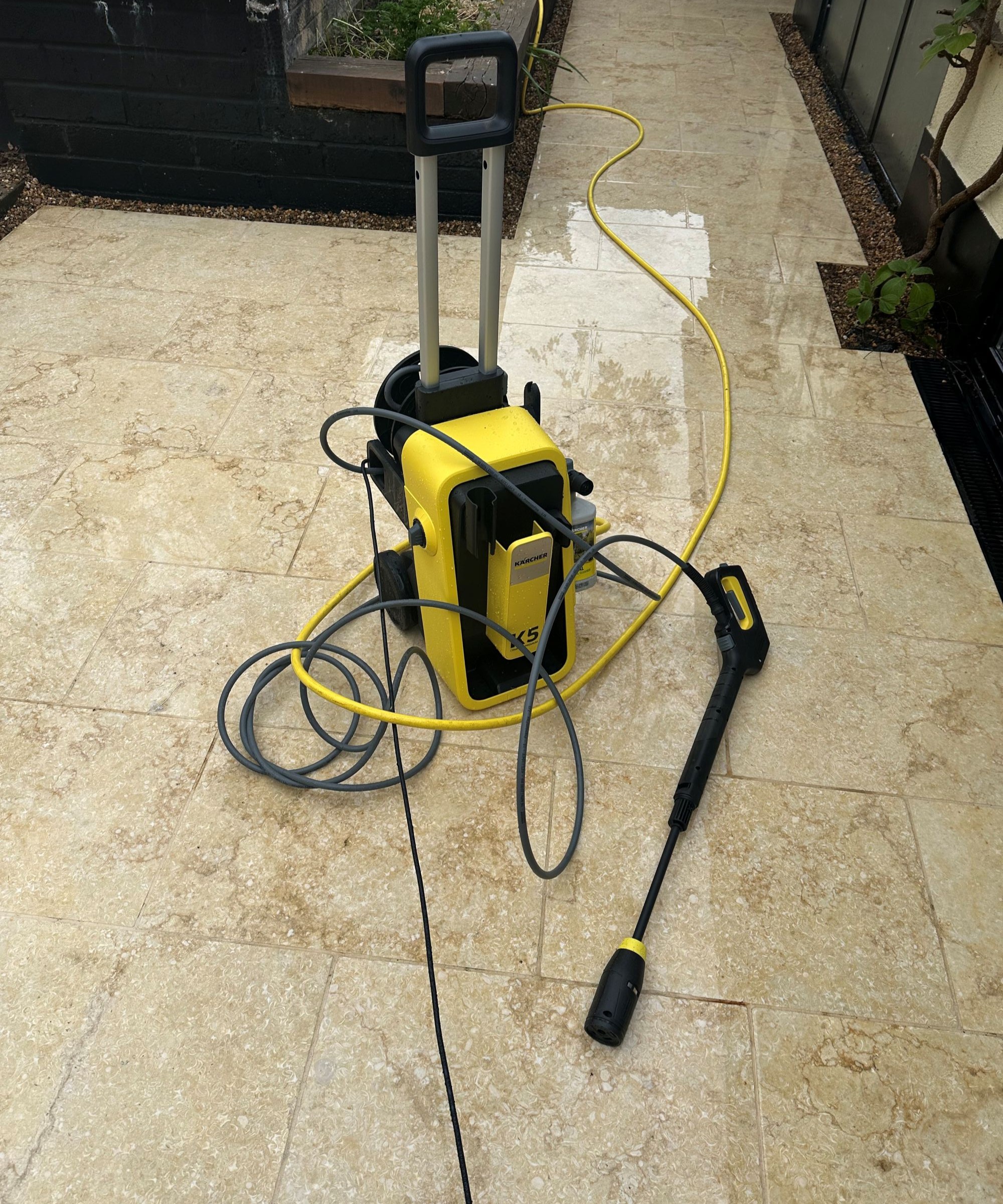 A yellow K&auml;rcher K5 Comfort Premium pressure washer on a cream limestone patio