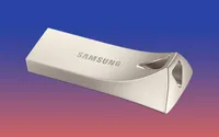 Product shot of the Samsung 32GB Bar USB Flash Drive MUF-32BE3/AM, a silver-colored flash drive with a built-in ring loop.