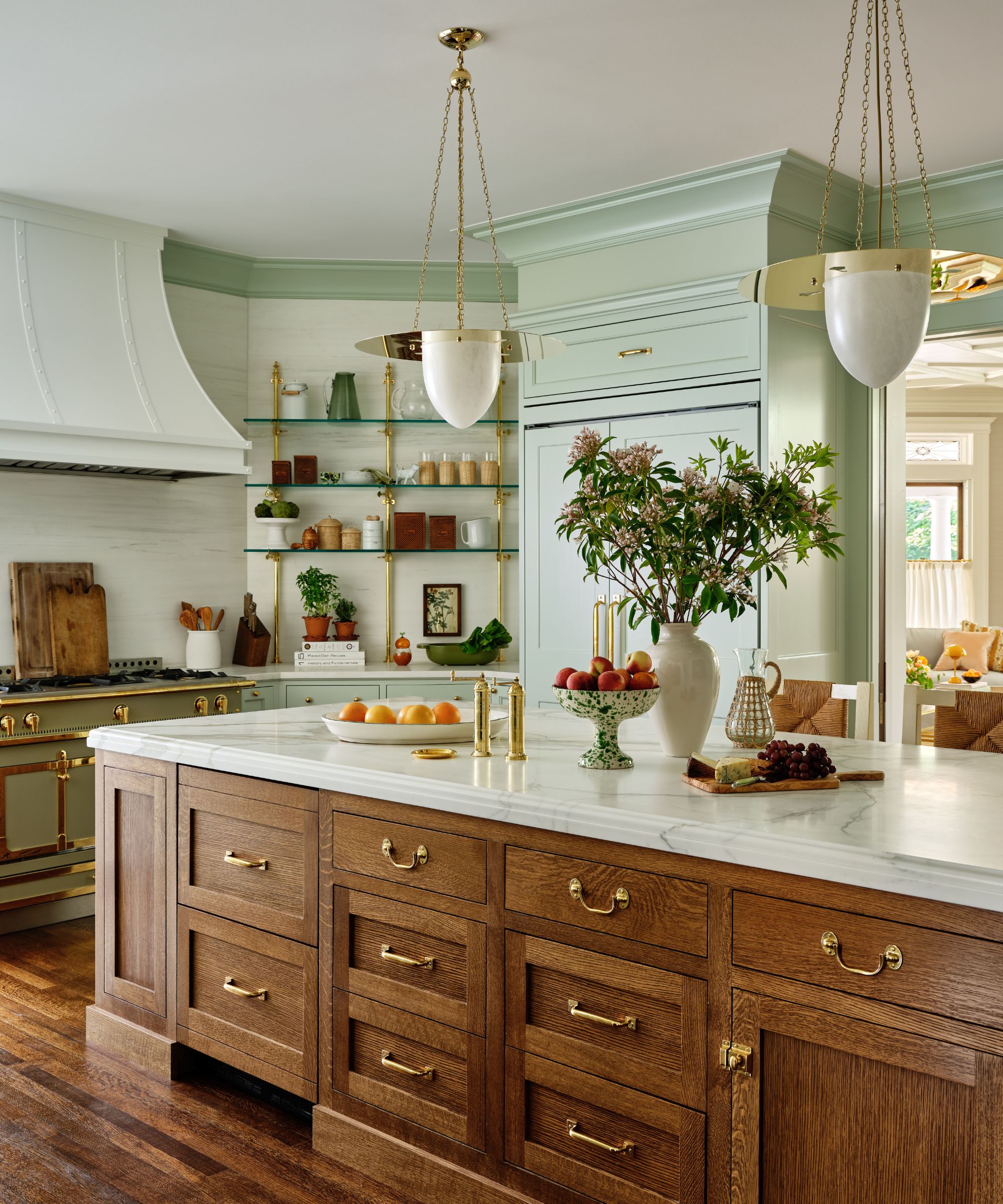 Traditional kitchen with mint green cabinetry and trim, a free-standing island with wooden drawers, gold hardware, a marble countertop, round pendant lights, and a mint range cooker and hood.