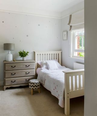 Grey childrens bedroom with wooden single bed and chest of drawers next to wall with star decorations on
