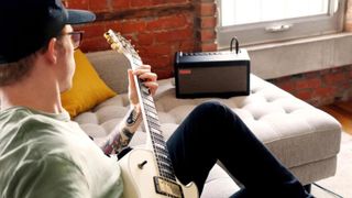 Man plays guitar with Positive Grid Spark amp on white sofa