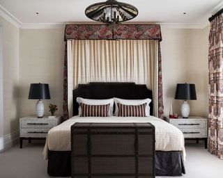 A grand canopy bed in a cozy bedroom with dark upholstery and pale cream walls.