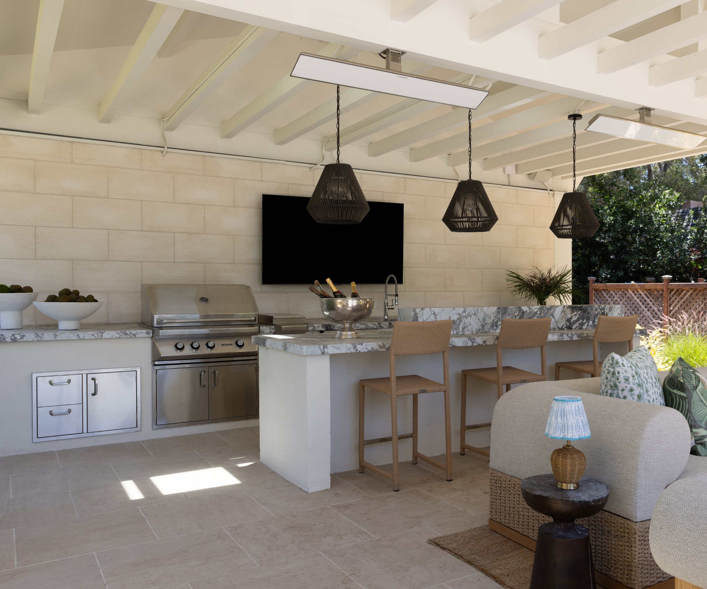 A covered outdoor kitchen with marble countertops and a connected living area