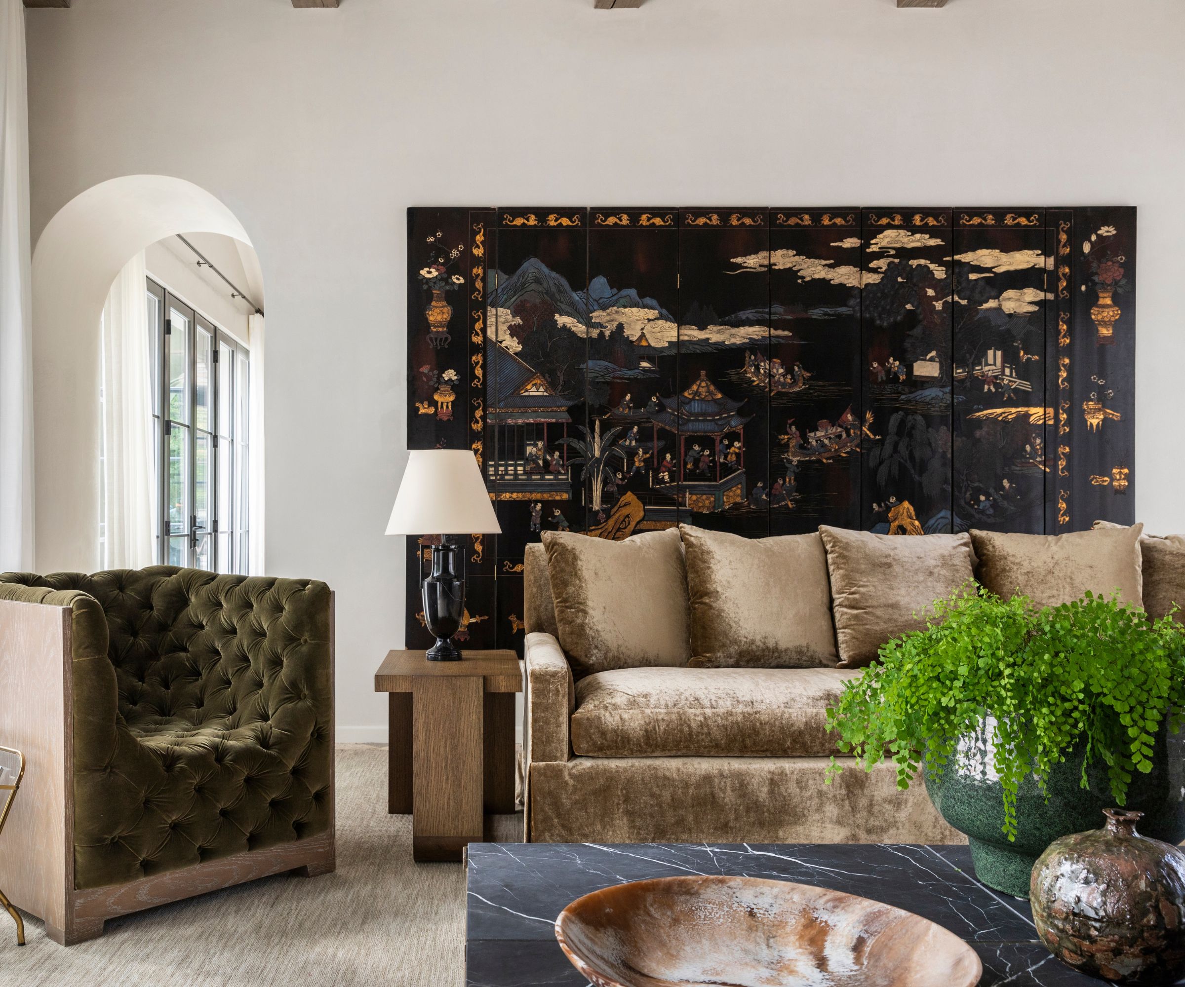 cozy fall living room with a velvet beige couch, marble coffee table, green velvet armchair and a large vintage chinese artwork behind