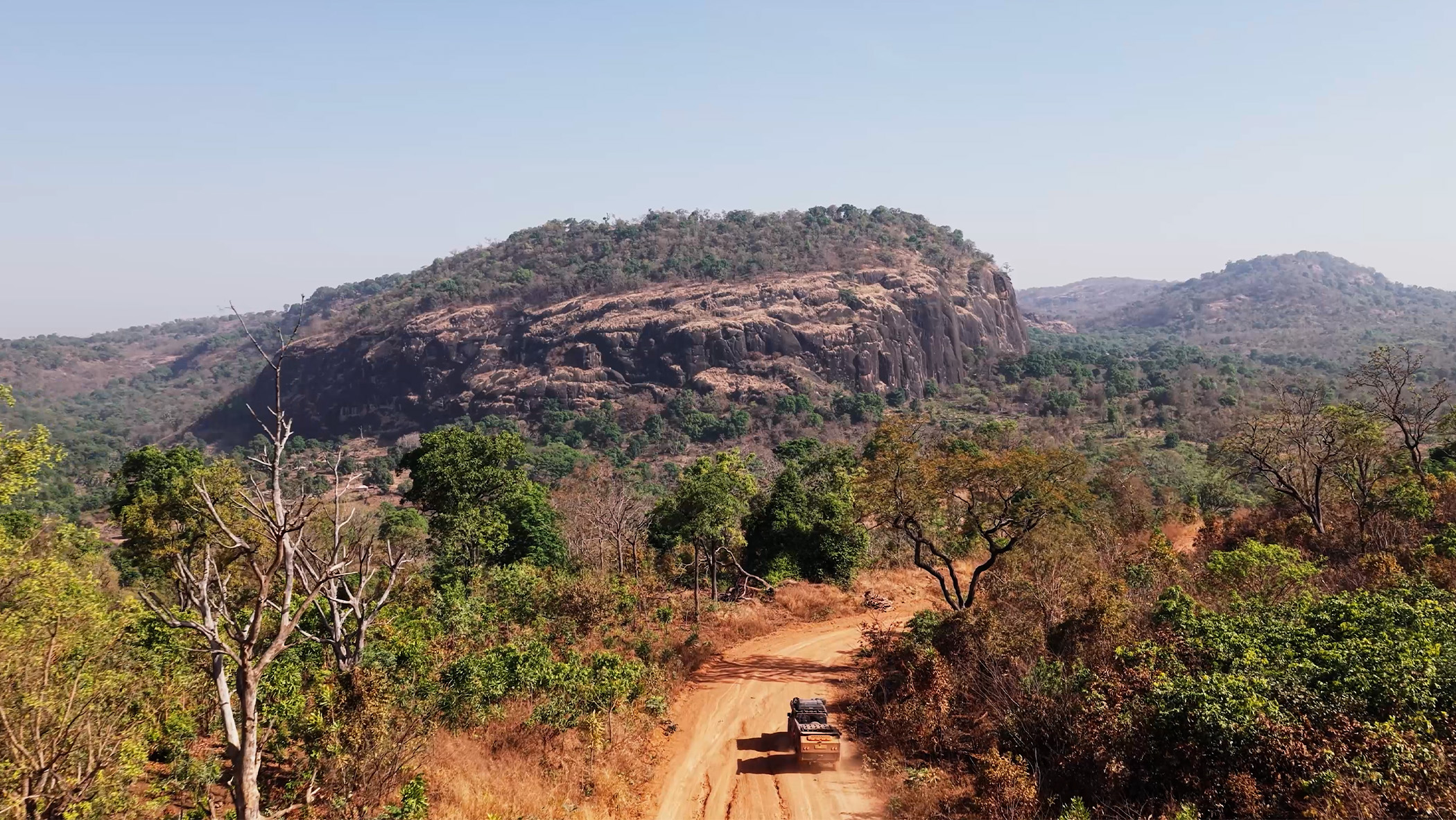 An aerial view of a car driving along a dusty road.