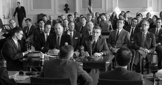 black-and-white photo of several dozen men in suits at a hearing.