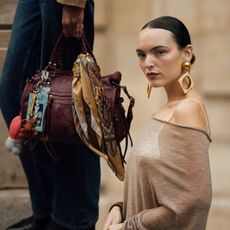 Burgundy leather bag with scarf and bag charms. Woman in gold dangly earrings. 