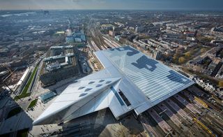 Daytime, aerial view of Rotterdam Central Station, surrounding landscape, buildings, roads, trees, cars, houses, rail tracks, blue sky