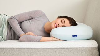 A woman lies asleep with her head resting on the Casper Hybrid Pillow with Snow Technology, both on a mattress