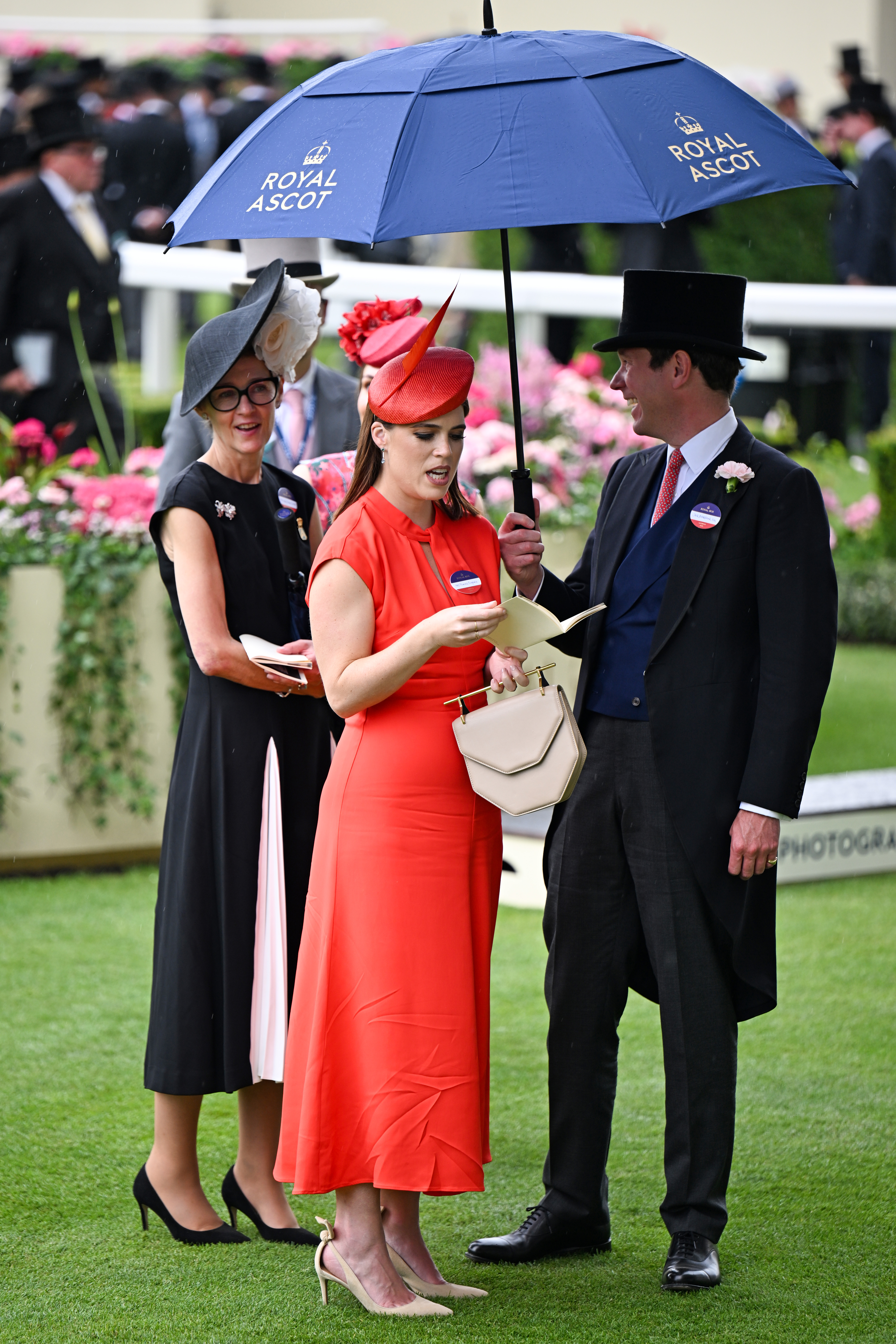 Princess Eugenie standing under an umbrella in a red dress with Jack Brooksbank at Royal Ascot