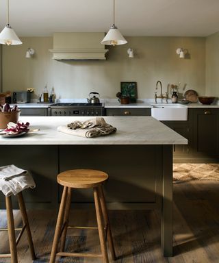 kitchen with dark brown cabinets, marble countertops, butler sink, brass faucet, wood stools, stone walls, pendant lights, wall lights, wooden floor