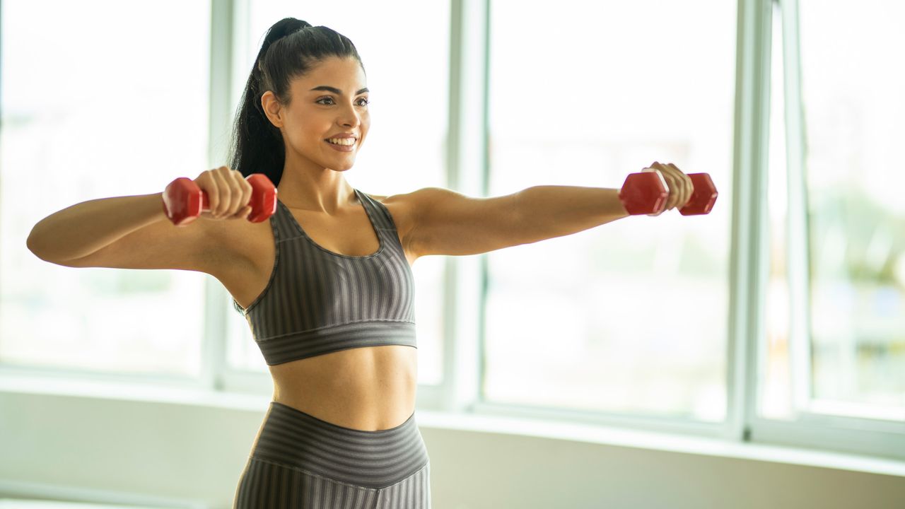 A woman performing lat raises with small dumbbells