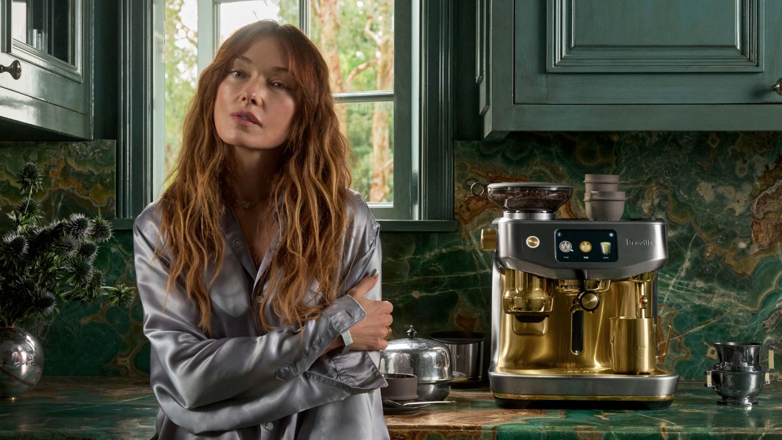 Kelly Wearstler in a green kitchen beside a Breville Mixed Metals silver and brass coffee maker
