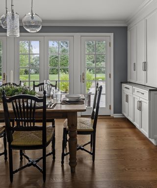 Dining table and chairs set for meal, pendant lights over, white kitchen cabinets, wood floor and doors to backyard