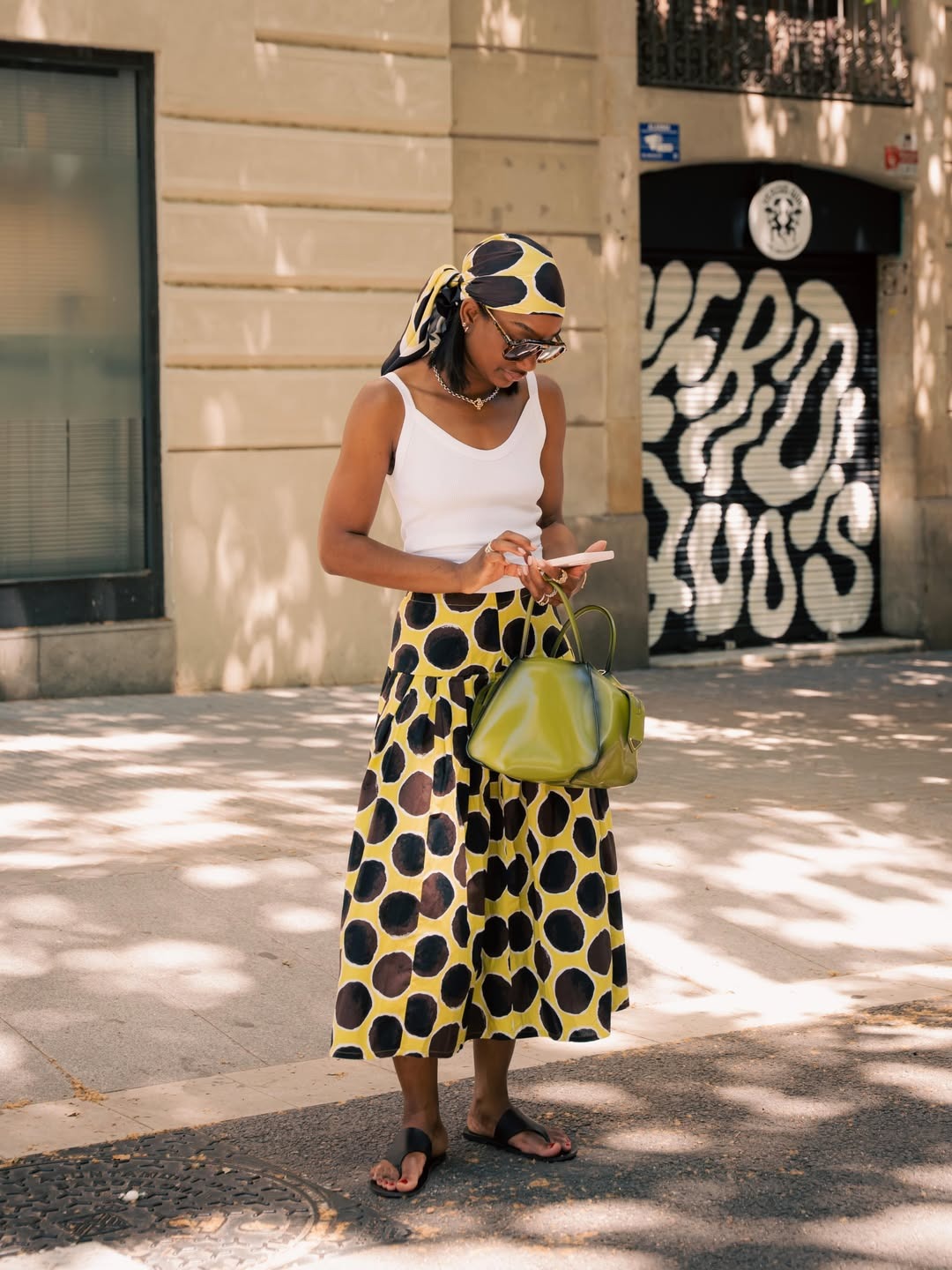 NYC woman wears a yellow and brown polka dot skirt with matching bandana and a white tank top.
