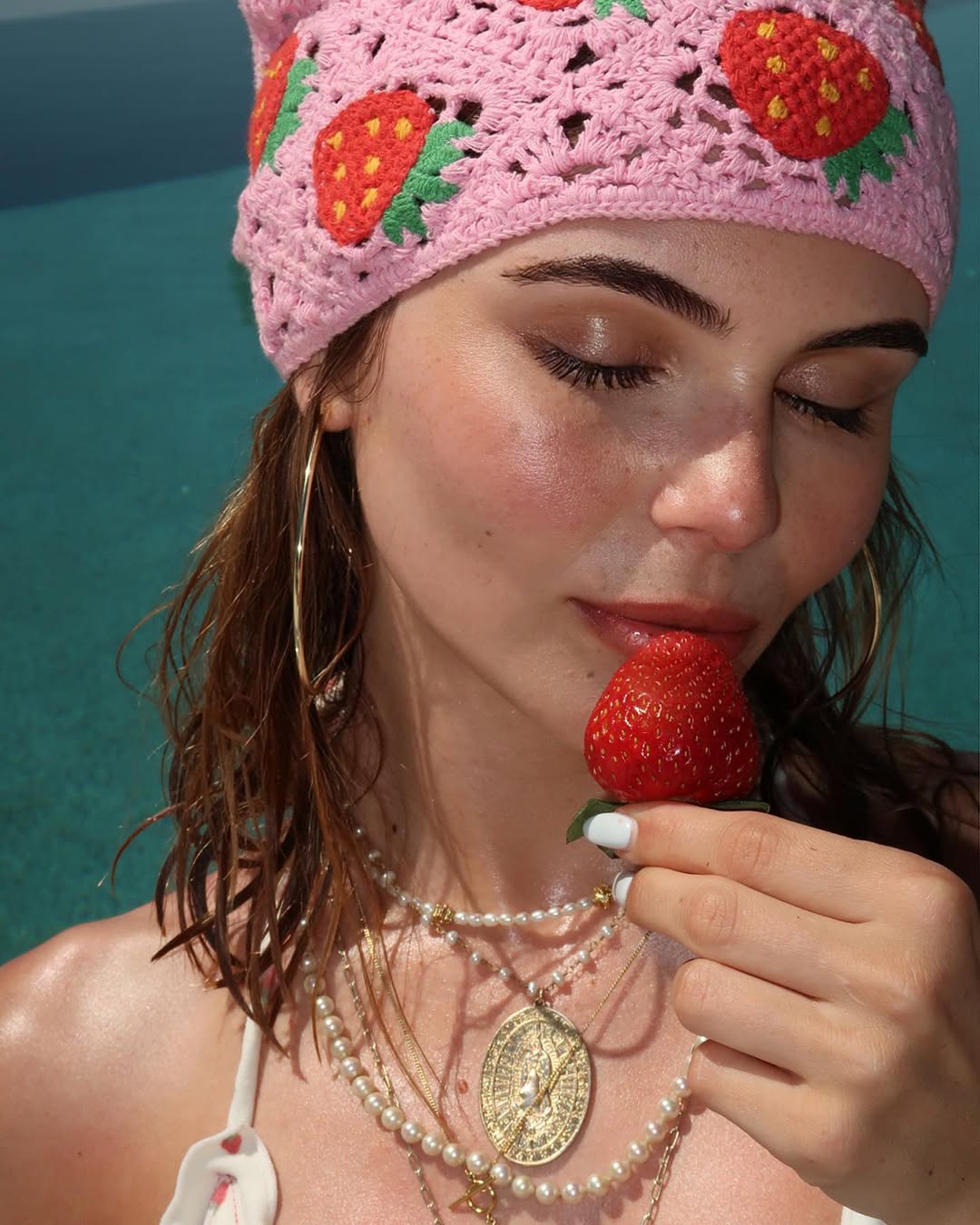 Olivia Jade poses with a subtle hint of blush and a diffused wash of eyeshadow holding a strawberry and wearing a ton of necklaces