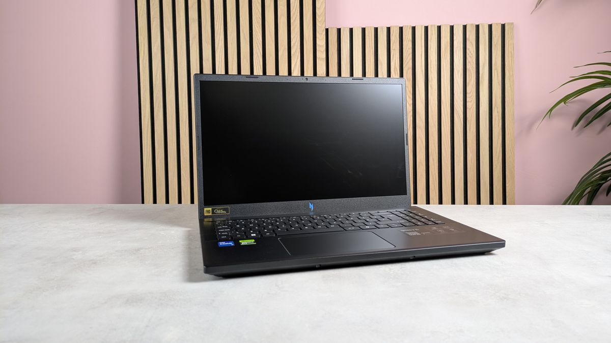 Acer Nitro V 15 open on desk with wooden panels, plant, and pink wall in background