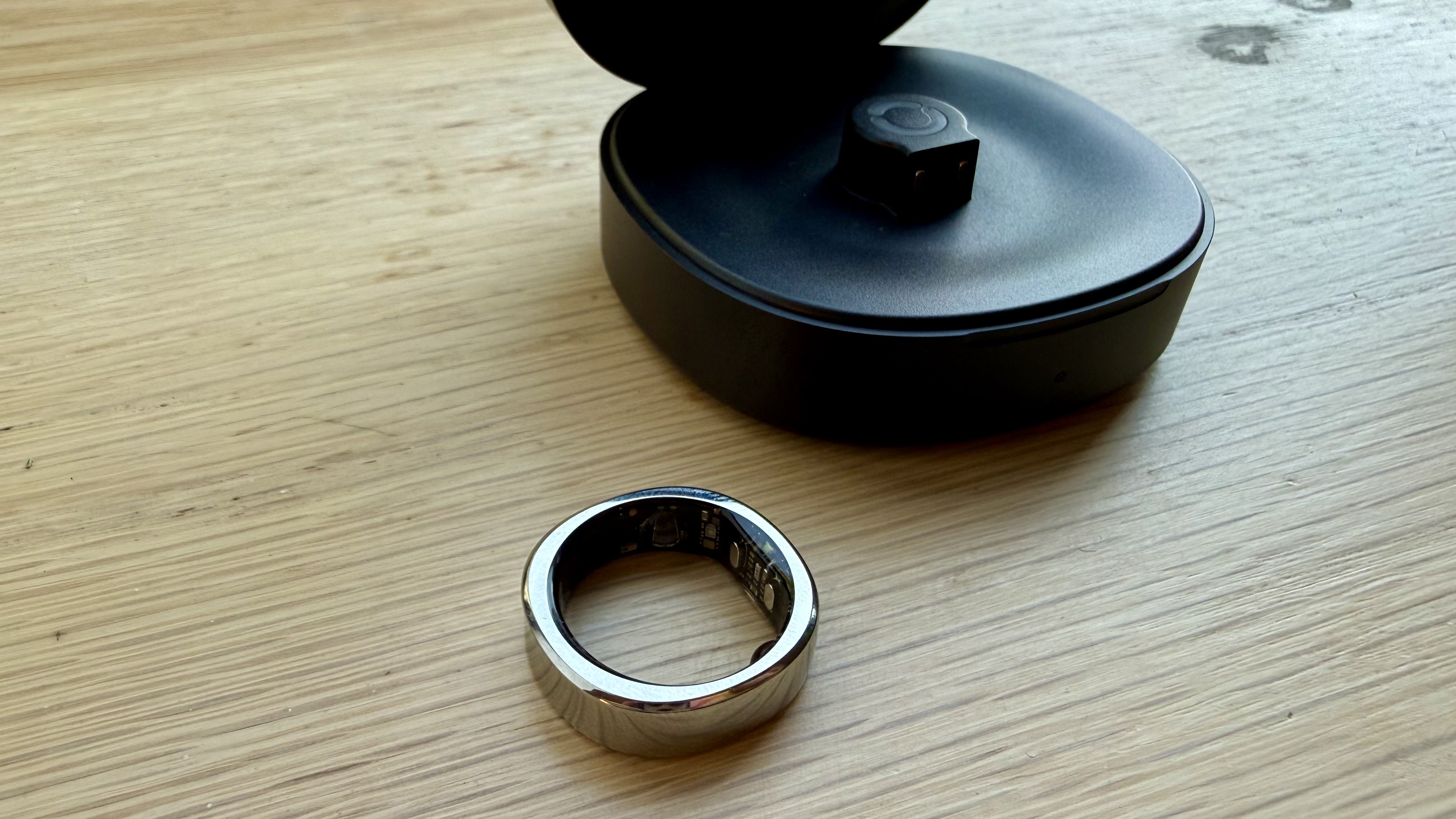 The RingConn Gen 3 smart ring in silver pictured with its case on a wooden surface