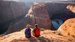 Two visitors sit facing the Grand Canyon