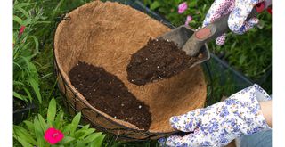 person preparing a hanging basket with a trowel adding compost to a liner as the first step of how to plant a summer hanging basket