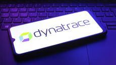 Dynatrace logo and branding pictured on a smartphone screen placed on top of a laptop keyboard in dimly lit room.