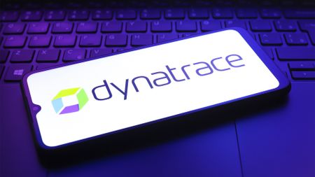Dynatrace logo and branding pictured on a smartphone screen placed on top of a laptop keyboard in dimly lit room.
