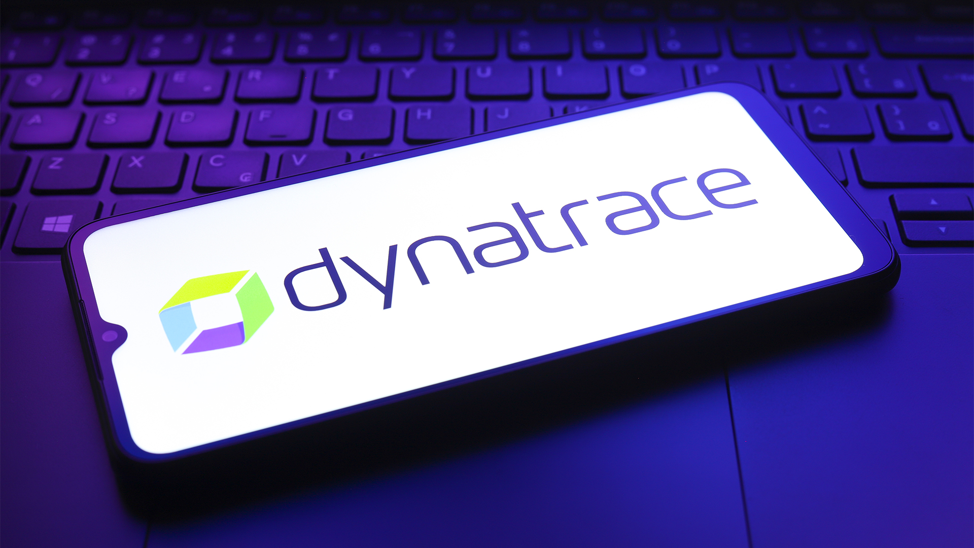 Dynatrace logo and branding pictured on a smartphone screen placed on top of a laptop keyboard in dimly lit room.