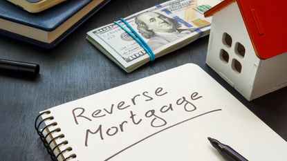 The words reverse mortgage are written on the page of a spiral notebook next to some cash and a calculator.