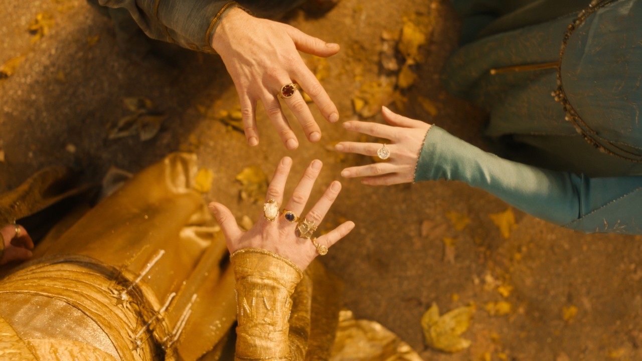 Three hands held up next to each other, forming a circle. They are all wearing one of the rings of power.