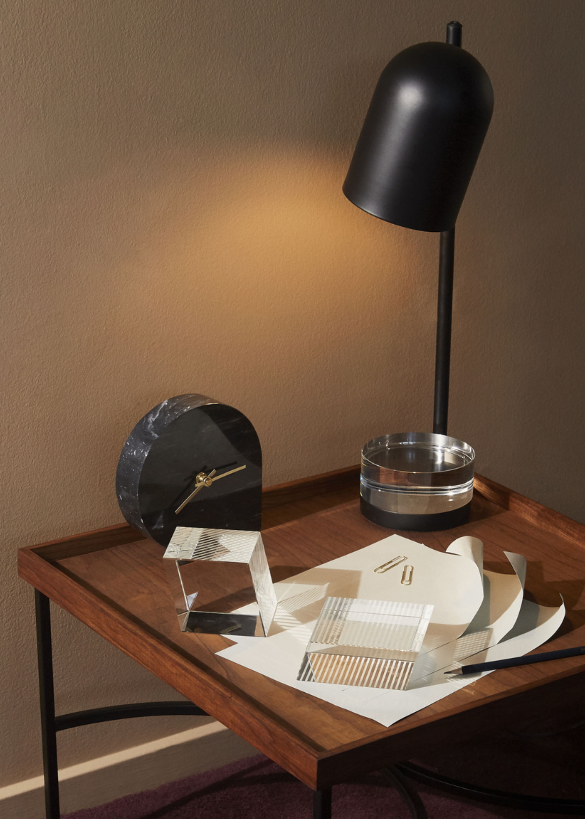 A black clock on a wood side table beside a table lamp