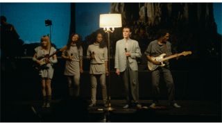 Tina Weymouth, Ednah Holt, Lynn Mabry, David Byrne, and Alex Weir stand together in front of a lamp in Stop Making Sense.