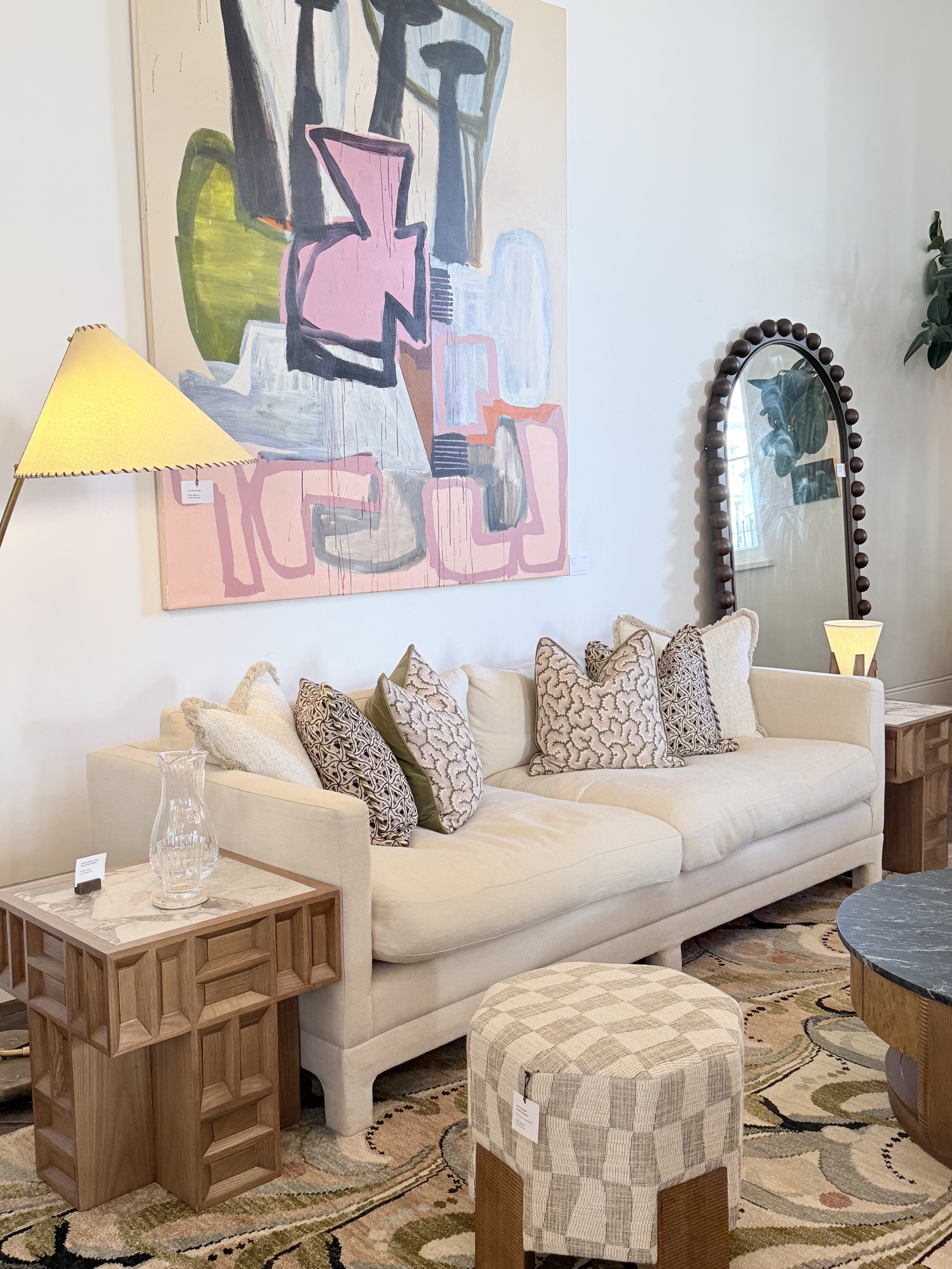 Soho Home Ashford sofa in showroom styled with cushions below large artwork, with timber side table, fabric ottoman, patterned rug and bobble mirror