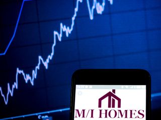 closeup of M/I Homes logo on smartphone with blue stock chart in the background