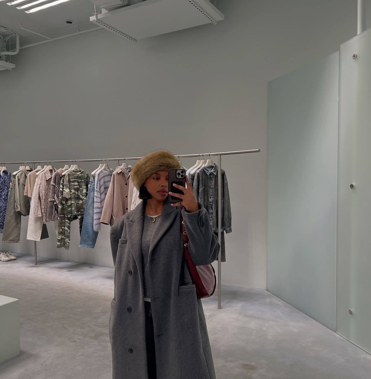 @aysha.sow wears a gray blazer, a gray sweater with a white tee underneath, a burgundy shoulder bag, and a fur hat.