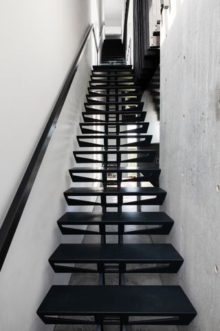 A large industrial style staircase with black step and hand rail and cement walls
