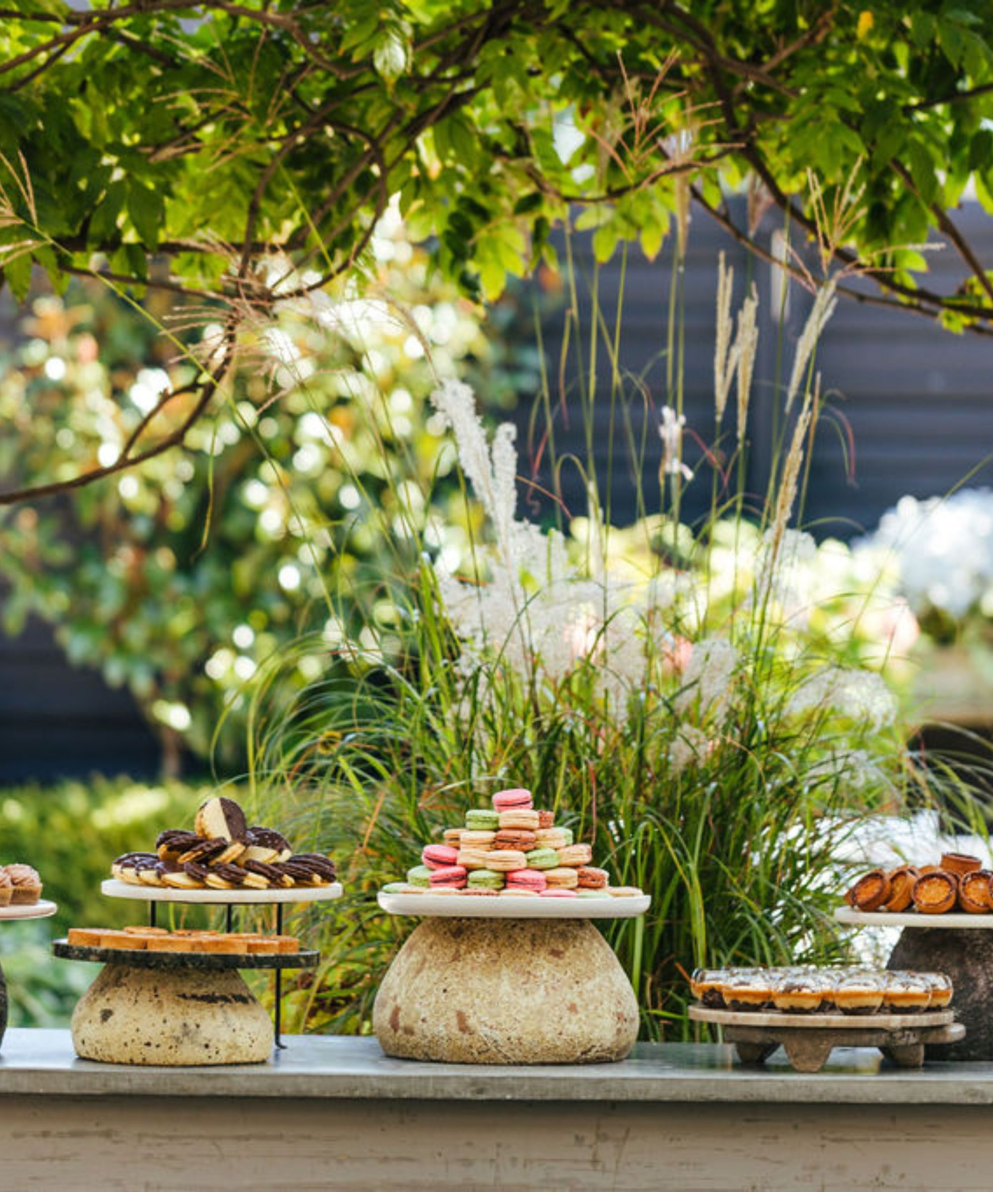 Outdoor table with plates of tarts, macarons and desserts on rustic display stands