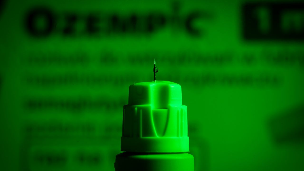 An Ozempic needle injection pen in front of a blurred green background 