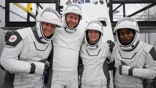 four astronauts in spacesuits clustered together and smiling at the camera