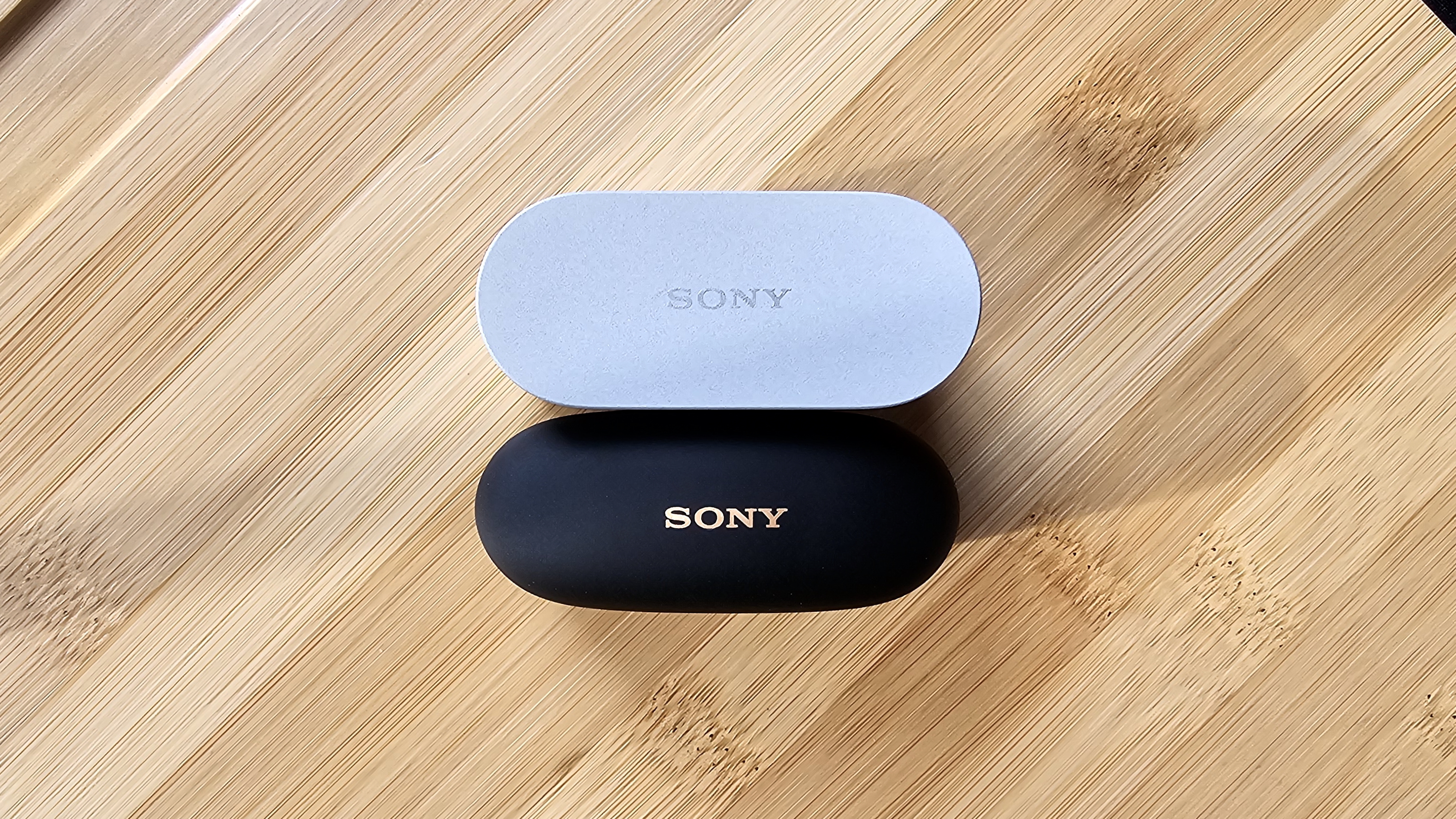 The Sony WF-1000XM6 and WF-1000XM5 side by side in a comparison, on a light wood table 