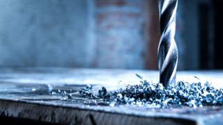 Silver metal drill drilling into sheet metal with shards of swarf around the drill bit