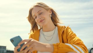 Woman wearing a yellow jacket holding a phone and smiling down at it