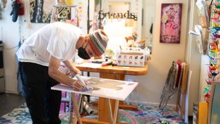 A man wearing a mask and beanie bends over a painting project