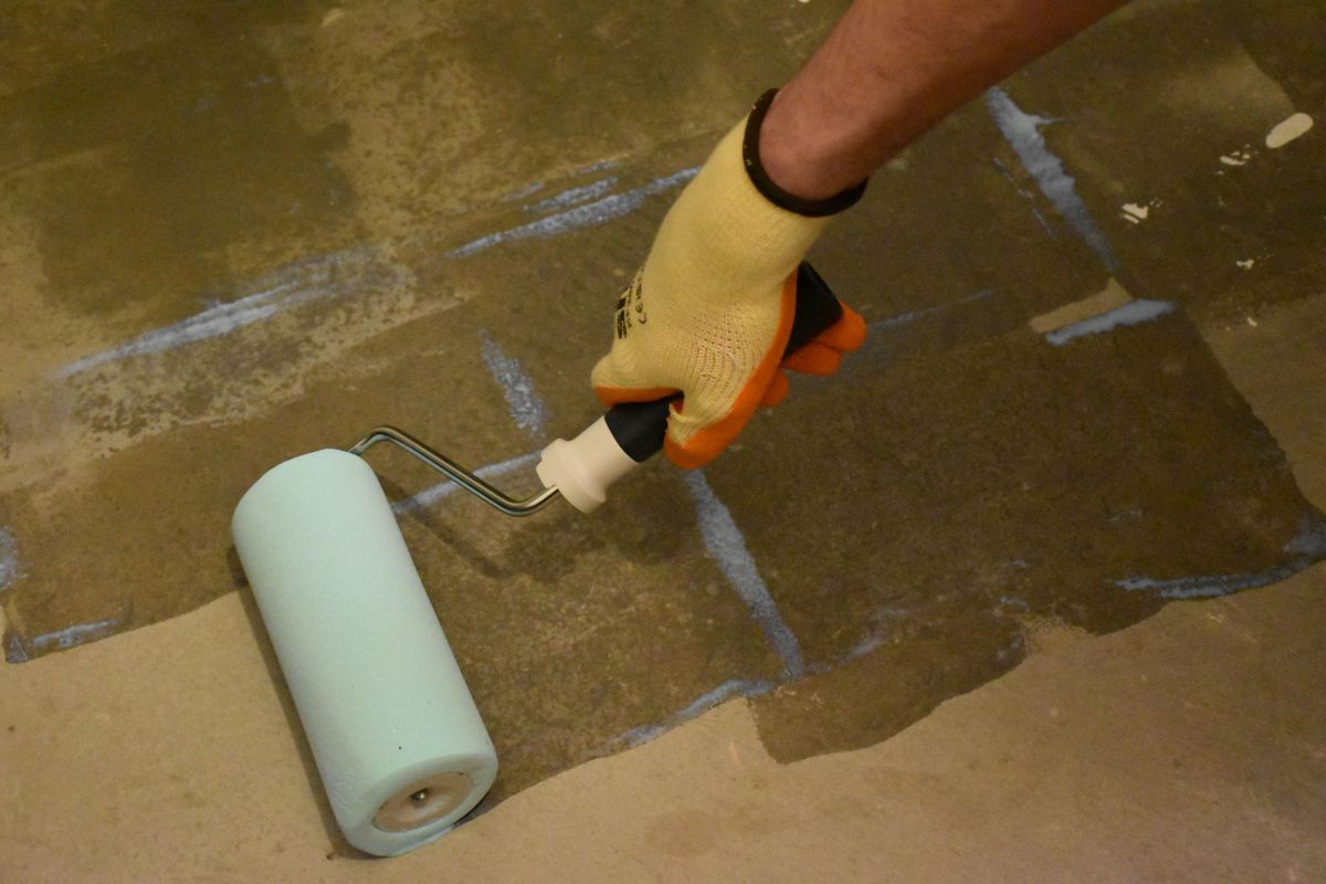 Rollering on a primer to the floor before sticking down herringbone wooden flooring